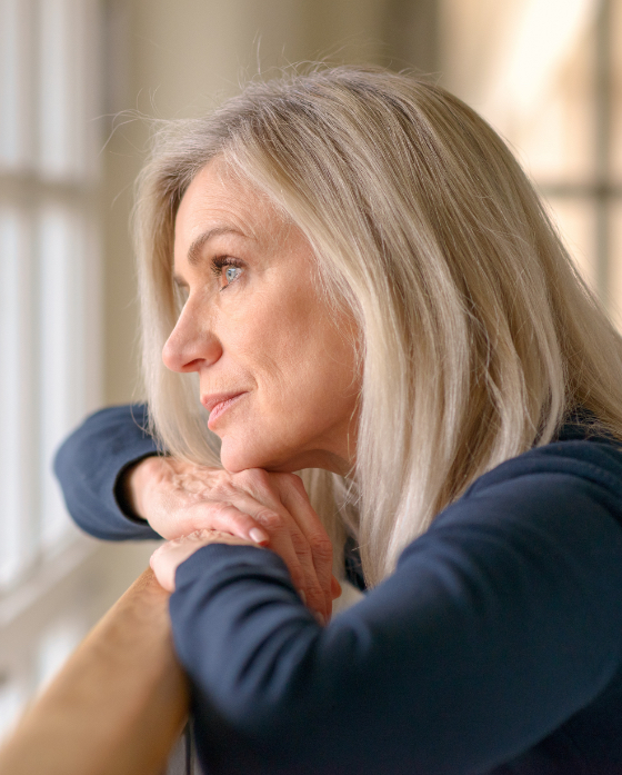 Older woman looking out the window of her house