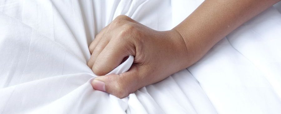 Woman's hand clutching bed sheets